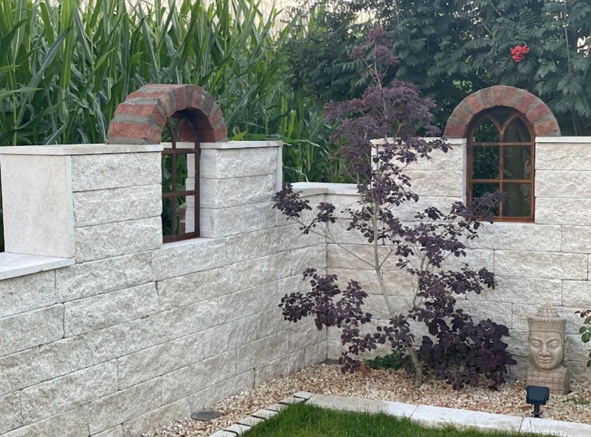 Weiße Mauer mit Bogenfenstern und Zierbaum bei Tag